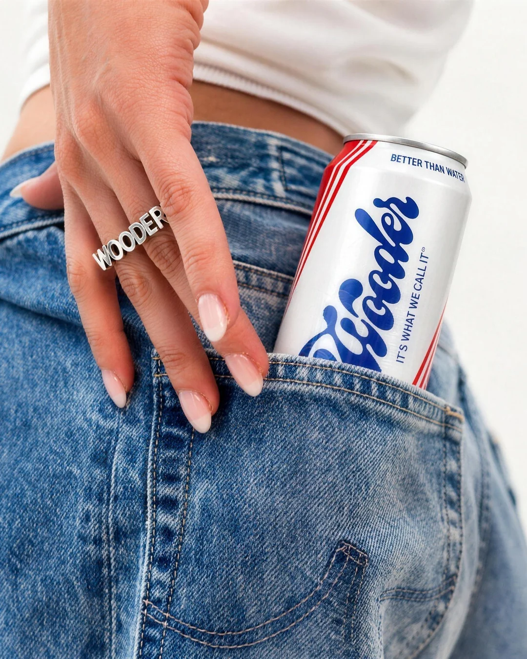A Wooder can tucked into a denim back pocket beside a hand wearing a Wooder ring